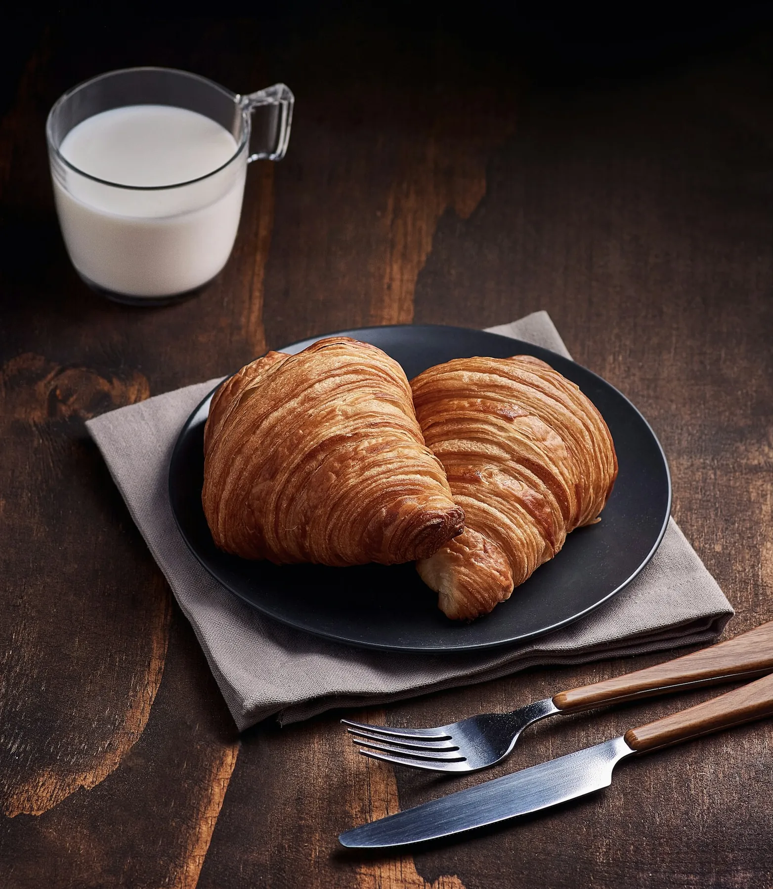 Croissant on a dark plate with a jug of milk