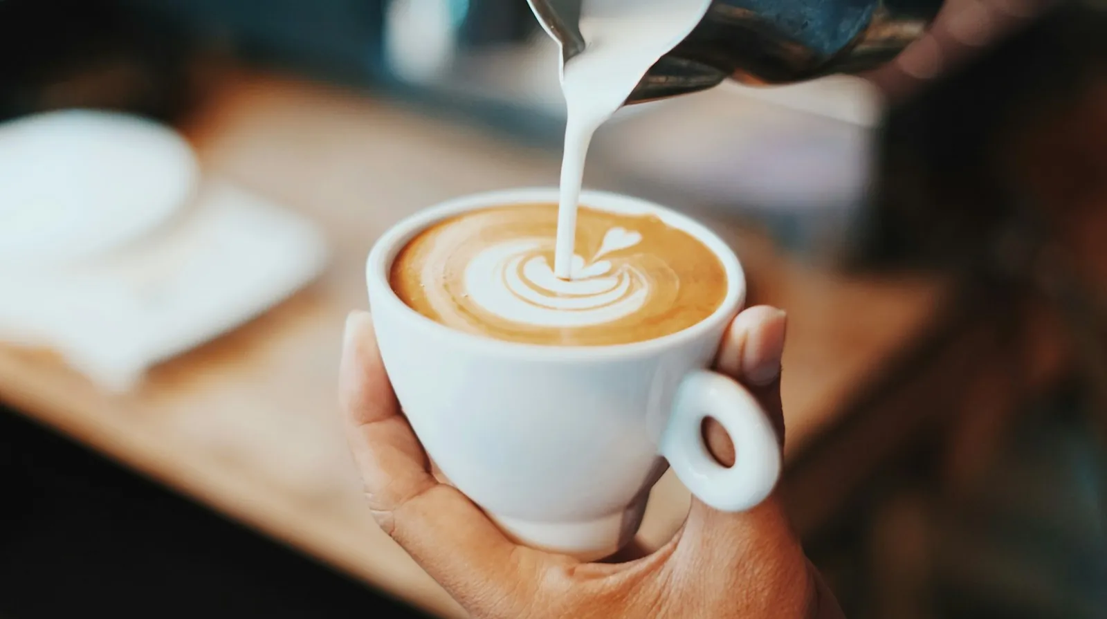 Barista pouring latte art into a white cup