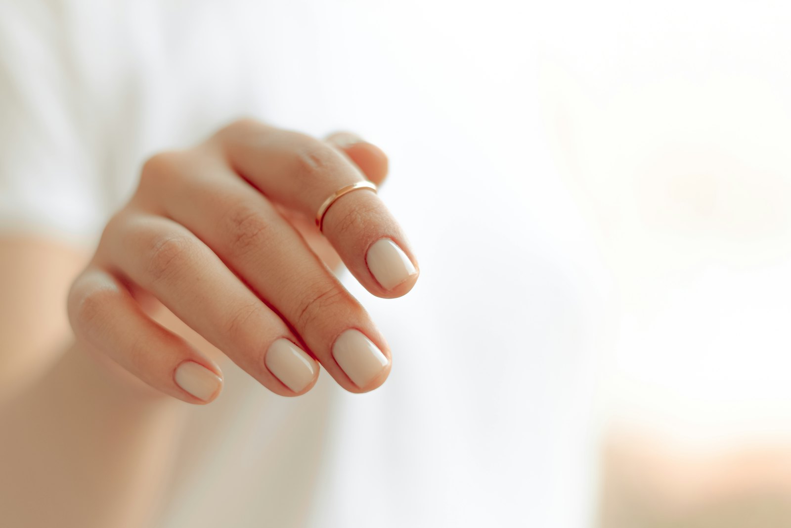 Hand with soft nude manicure and a thin gold ring