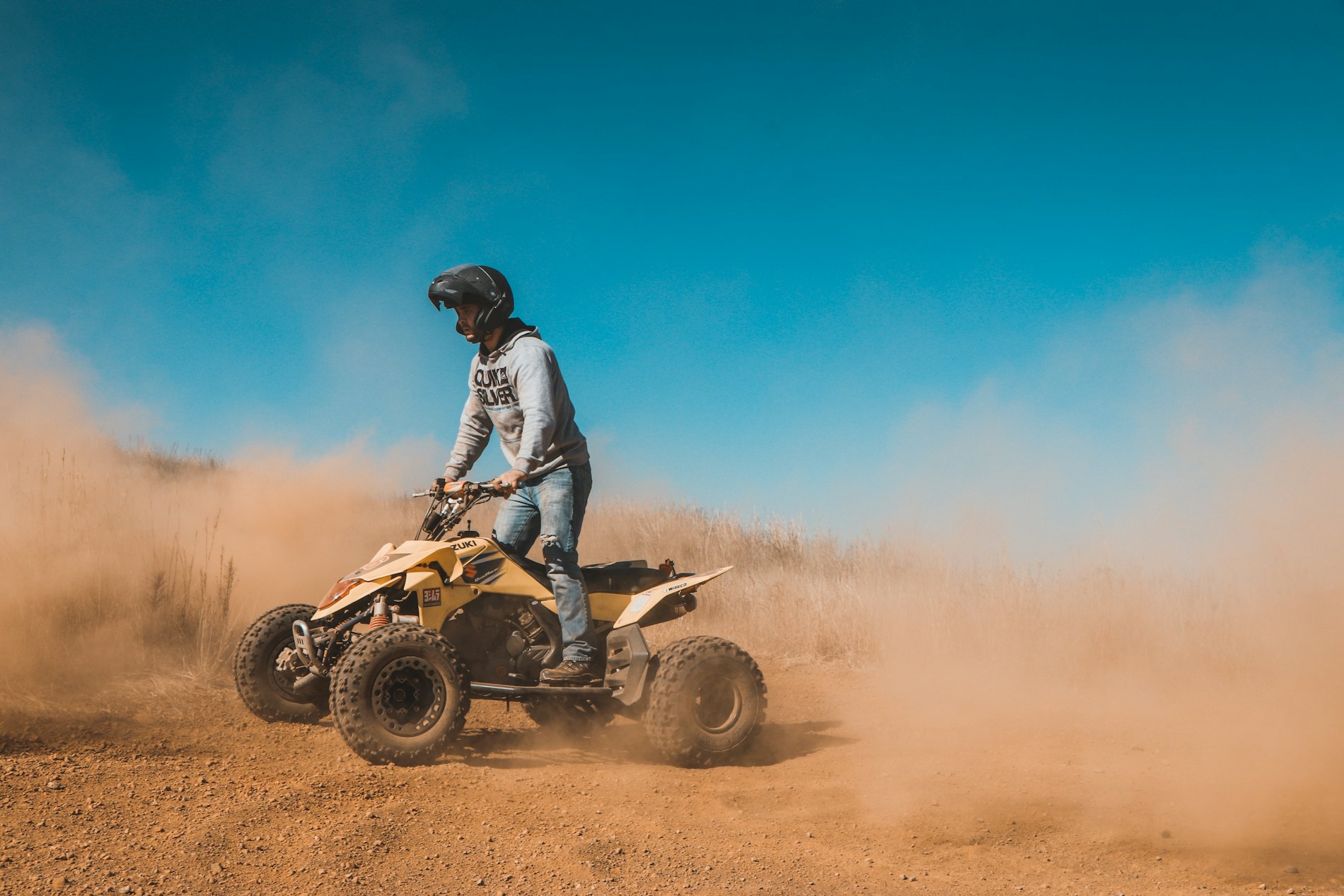 Rider on a quad bike kicking up a cloud of dust under a blue sky